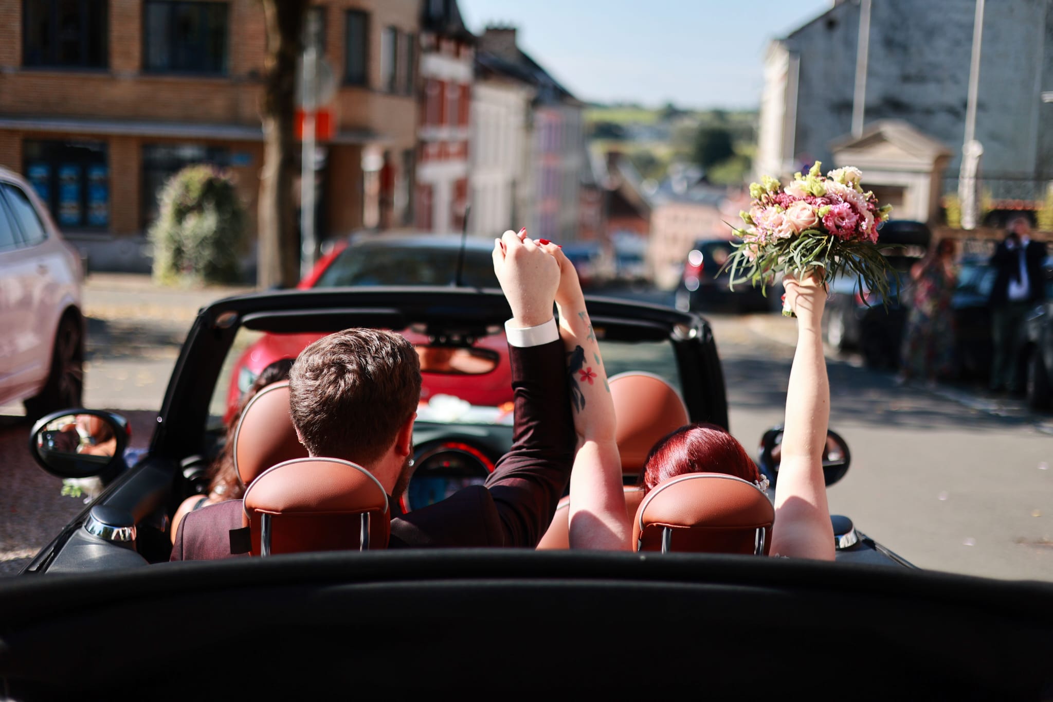 Les mariés de dos en décapotable, bouquet levé
